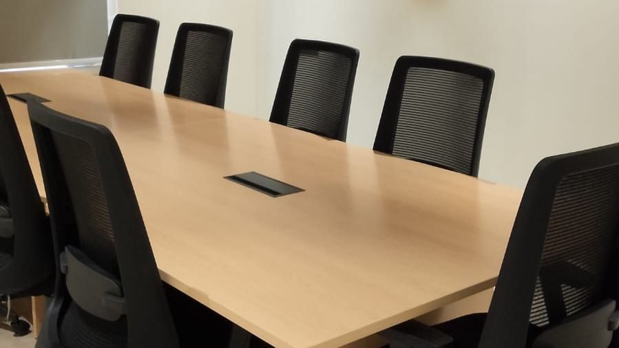 Conference room with a long wooden table surrounded by black mesh office chairs on wheels.
